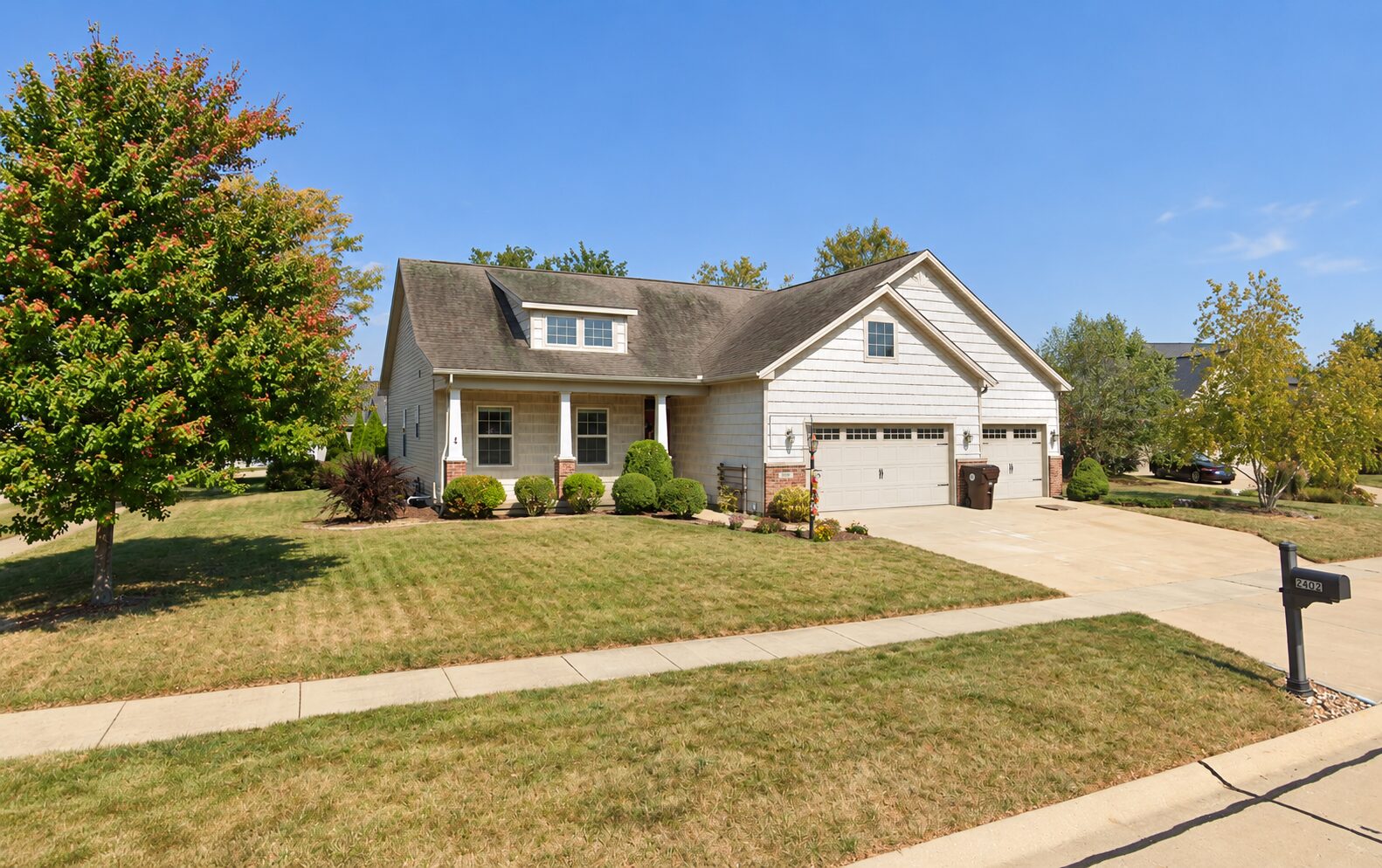 A light grey craftsman home in Mahomet before treatment, its asphalt shingle roof mottled with dark green-grey algae streaking and faded, worn granules